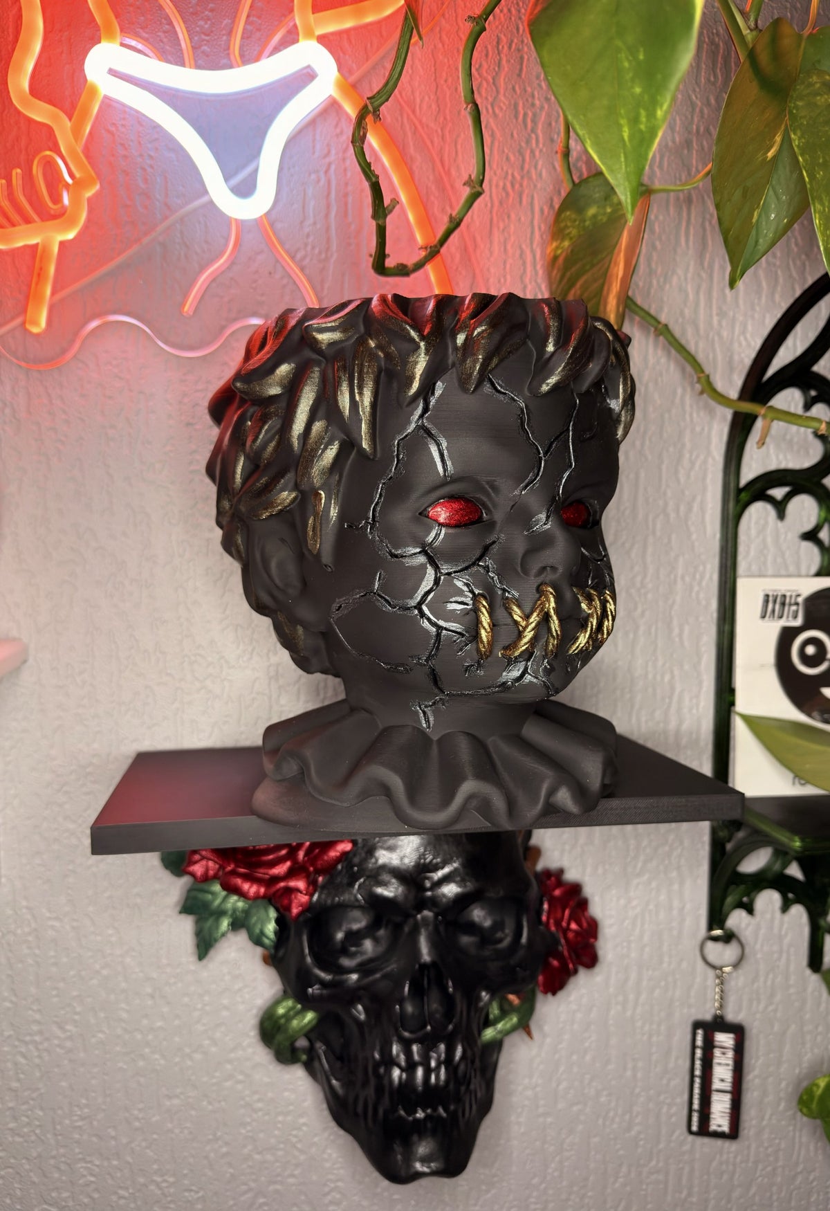 Hollow Child gothic doll head planter in matte black with cracked face, red eyes and gold stitched mouth, holding a trailing plant