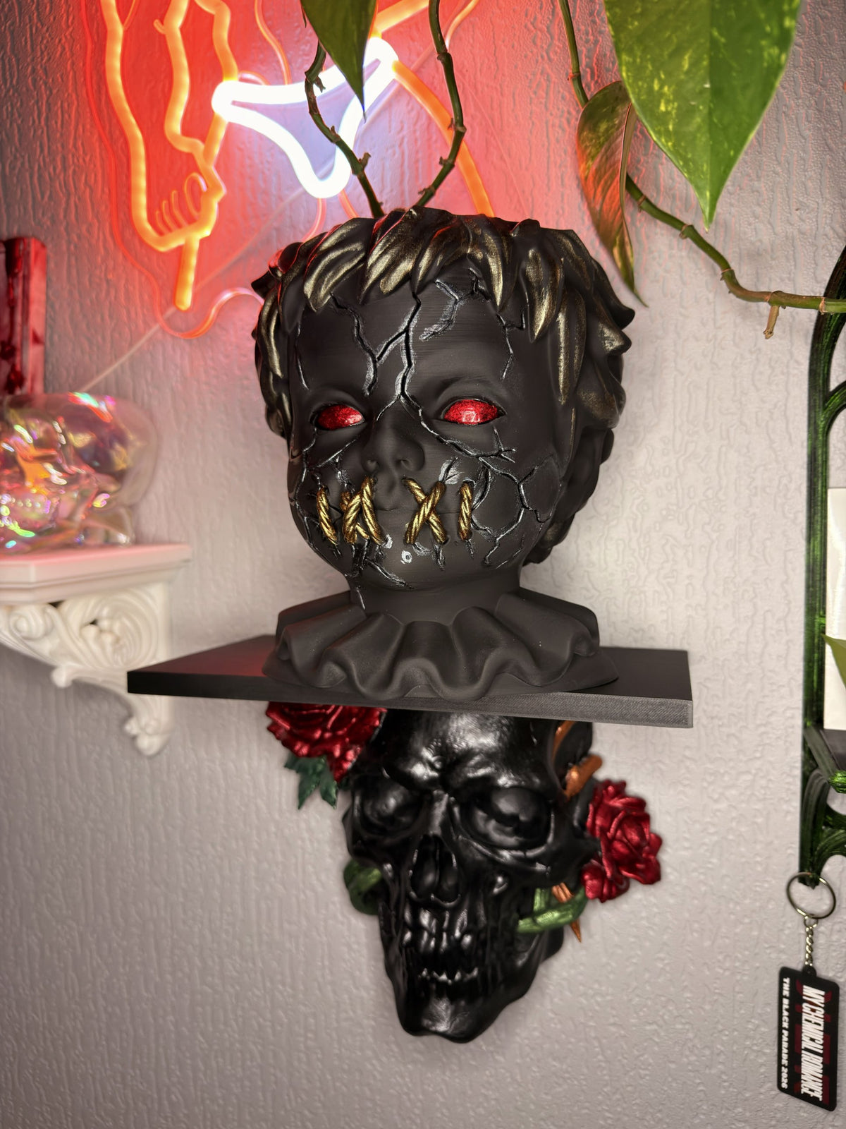 Hollow Child gothic doll head planter in matte black with cracked face, red eyes and gold stitched mouth, holding a trailing plant