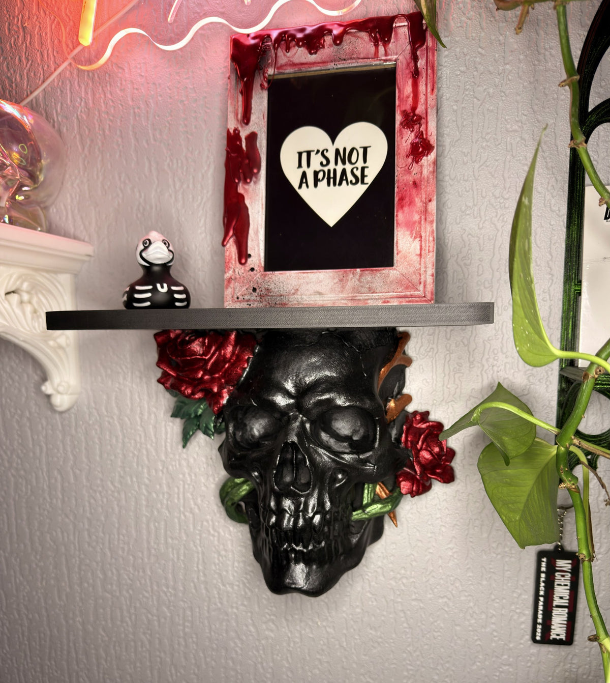 Thorn & Bone gothic skull wall shelf in glossy black with crimson roses, green vines and copper thorns, holding a framed print